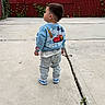 Hanzel Aquino is registered to the contest to win money with this photo: child, toddler, outdoors, sidewalk, standing, back_view, blue_sweatshirt, jeans, sneakers, racing_car, cars_theme, red_fence, brick_wall, chain_link_fence, vines, urban, residential, pavement, street_scene, daylight