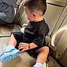 child, toddler, boy, car, car_interior, leather_seat, seated, black_shirt, black_shorts, sneakers, blue_shoes, bottle, short_hair, side_profile, passenger, vehicle, seatbelt, portrait, indoors, casual
