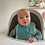 baby, high_chair, bib, blue_eyes, infant, child, hand, surprised_expression, clothing, indoor, person, seat, young_child, face, head, skin, furniture, babywearing, cute, portrait