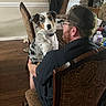 Nala is registered to the contest to win money with this photo: australian_shepherd, beard, brown_hair, camo_cap, casual_clothing, chair, collar, curious, dog, furniture, glasses, holding, indoor, man, pet, relaxed, seated, table, water_bottle, wood_floor