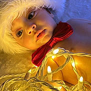 Jalei is registered to the contest to win money with this photo: adorable, baby, celebration, child, christmas_lights, close_up, cute, decorations, face, festive, glowing_lights, holiday, indoors, infant, laying_down, portrait, red_bow_tie, santa_hat, soft_blanket, warm_lighting