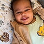 animal_pattern, baby, bed, blanket, buttoned_clothing, child, clothing, cute, expression, face, happy, indoors, infant, jacket, lion_print, lying_down, onesie, portrait, smiling, young_child