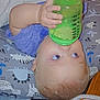 baby, child, blue_eyes, sippy_cup, pillow, blanket, lying_down, infant, hand, face, curious, indoor, soft_toys, baby_essentials, bottle, clothing, skin, head, young_child, cute