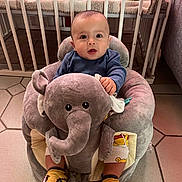 Maé a rejoint le concours — aidez-le/la à gagner de superbes lots ! baby, child, plush_toy, elephant, socks, yellow, nursery, crib, toy, floor_tiles, clothing, cute, indoor, infant, seated, soft_toy, expression, person, furniture, room