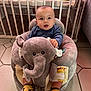 baby, child, plush_toy, elephant, socks, yellow, nursery, crib, toy, floor_tiles, clothing, cute, indoor, infant, seated, soft_toy, expression, person, furniture, room