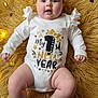 arms, baby, celebration, chubby, confetti, cute, face, fairy_lights, fluffy_rug, happy, indoors, infant, legs, lying_down, new_year, onesie, portrait, smiling, white_clothing, yellow_rug