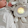 Haroun a rejoint le concours — aidez-le/la à gagner de superbes lots ! baby, infant, pajamas, plush_toy, bunny, bed, blanket, glowing, light, cute, sleepwear, child, soft_toy, comfort, indoor, laying_down, white_clothing, star_pattern, toddler, young_child