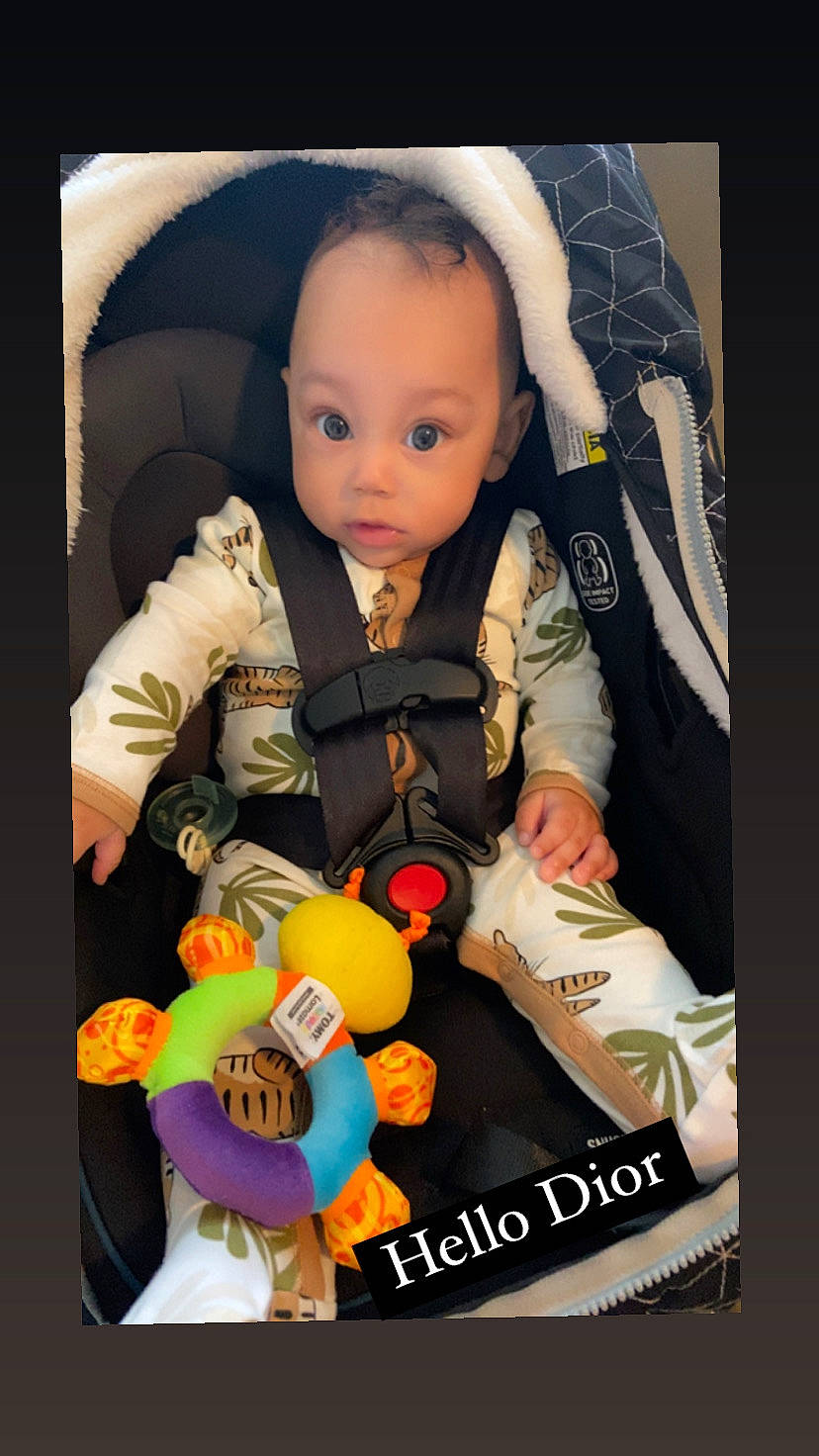 Dior is registered to the contest to win money with this photo: arm, baby, baby_carriage, baby_products, baby_toddler_clothing, baby_toys, car_seat, carmine, cheek, child, doll, hand, lap, person, plastic, product, room, sitting, stuffed_toy, surprise