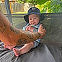 baby, child, hat, bucket_hat, tattoo, arm, outdoor, cushion, gray_cushion, greenery, plants, fence, wooden_fence, striped_outfit, feet, hands, person, summer, portrait, happy