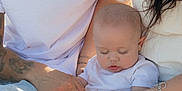 Feonix is registered to the contest to win money with this photo: baby, infant, sleeping, family, hand_holding, casual_clothing, jeans, white_shirt, bracelet, tattoo, outdoor, natural_light, close_up, parent, mother, father, skin, barefoot, candid, love