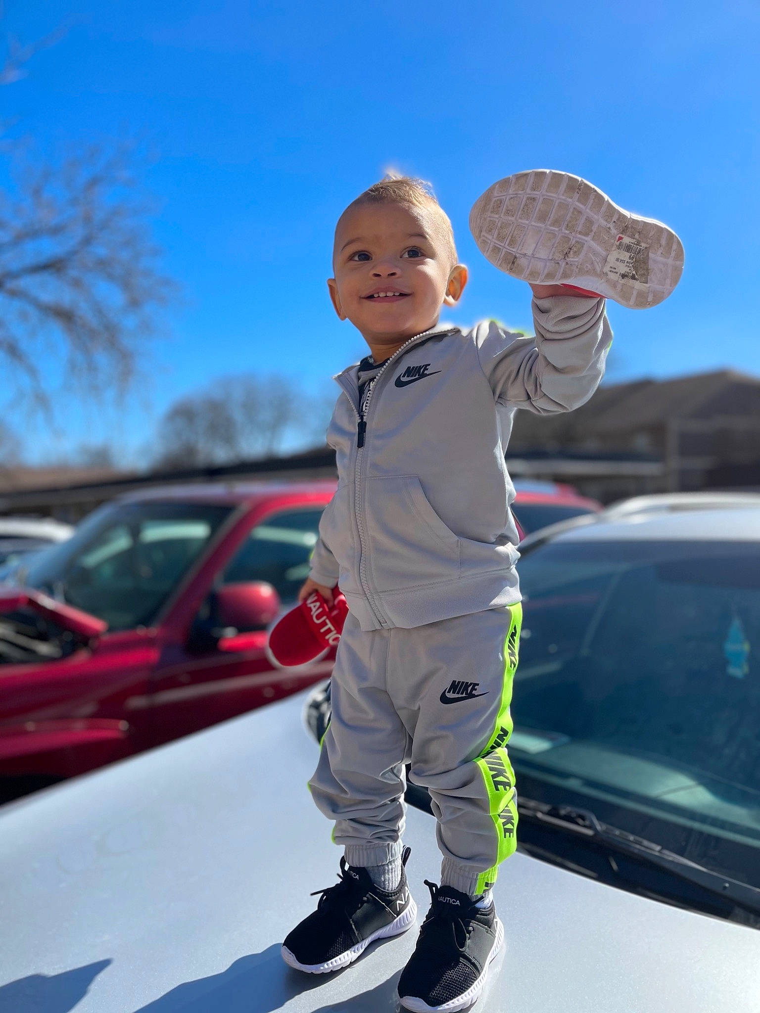 Irie is registered to the contest to win money with this photo: automotive_design, automotive_exterior, automotive_lighting, automotive_tire, bumper, car, fun, gesture, happy, hat, hood, joy, leisure, motor_vehicle, person, recreation, sky, standing, toddler, tree