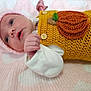 baby, infant, pink_blanket, knitted_hat, crocheted_outfit, pumpkin_patch, soft_texture, lying_down, cute, small_fist, wide_eyes, white_sleeves, close_up, adorable, newborn, warm_clothing, indoors, portrait, face, child