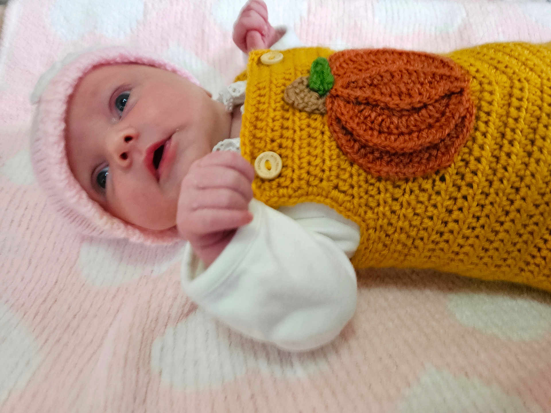 Maeve joined the competition — help win amazing prizes! baby, infant, pink_blanket, knitted_hat, crocheted_outfit, pumpkin_patch, soft_texture, lying_down, cute, small_fist, wide_eyes, white_sleeves, close_up, adorable, newborn, warm_clothing, indoors, portrait, face, child