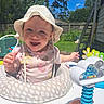 Serena joined the competition — help win amazing prizes! baby, child, hat, sun_hat, onesie, polka_dots, baby_ring, toys, outdoor, sunny, greenery, grass, fence, smiling, happy, portrait, face, playtime, summer, daytime