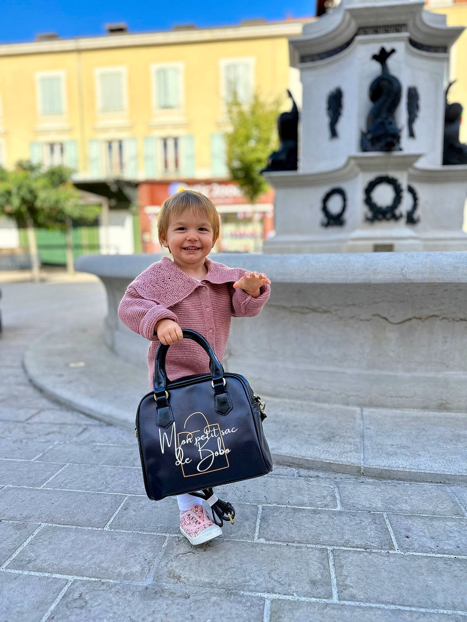 Alyah participe au concours pour gagner de l'argent avec cette photo : bag, child, city, electric_blue, fashion_accessory, happy, joy, leisure, luggage_and_bags, magenta, pattern, person, plant, recreation, sitting, sky, sleeve, smile, toddler, travel