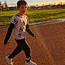 boy, child, running, outdoor, track, grass, sunlight, shadow, sky, casual_clothing, sneakers, long_sleeves, tshirt, park, daytime, nature, motion, youth, active, recreation