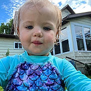 Lyndi is registered to the contest to win money with this photo: toddler, child, face, portrait, outdoor, sky, clouds, house, window, grass, water_spray, swimsuit, wet_hair, blue, purple, pattern, person, summer, daylight, nature