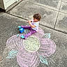 Alaiyah is registered to the contest to win money with this photo: child, toddler, curly_hair, chalk, sidewalk, flower, drawing, outdoor, concrete, box, toy, purple_pants, socks, white_shirt, grass, door, house, play, creative, happy