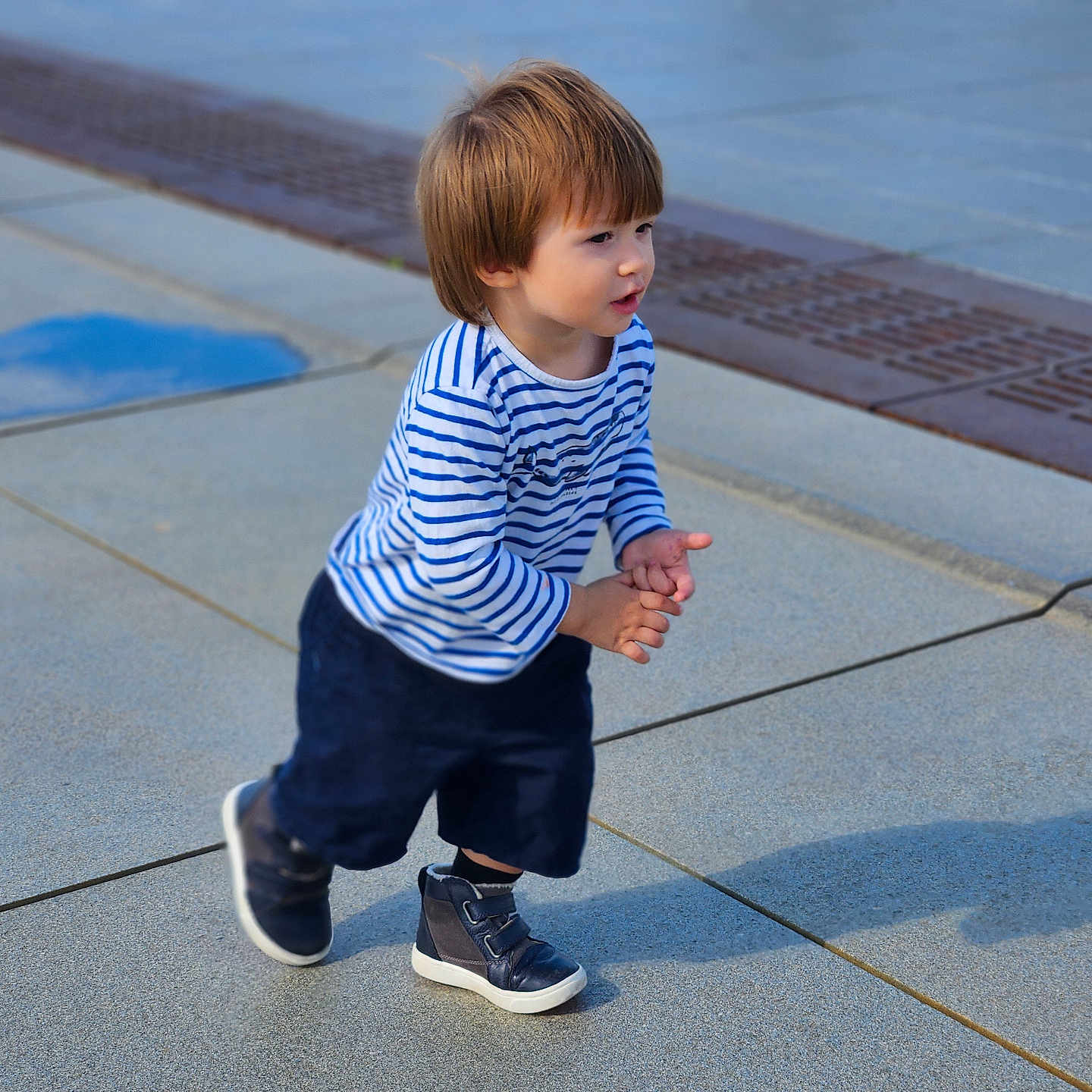 Meyer Pickett participe au concours pour gagner de l'argent avec cette photo : active, blue_shoes, casual_clothing, child, concrete, curly_hair, daylight, navy_shorts, outdoor, pavement, playful, puddle, reflection, shadow, sideview, sneakers, striped_shirt, toddler, walking, young_child