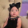 Carmen joined the competition — help win amazing prizes! baby, child, face, headband, black_bow, pucker, cushion, chair, black_dress, embroidery, skin, arm, portrait, indoor, cute, infant, seated, expression, young, person
