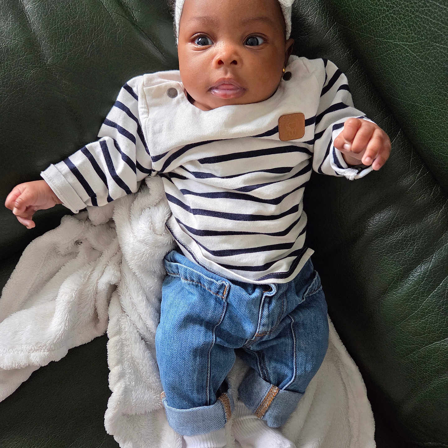Koffi Havilah participe au concours pour gagner de l'argent avec cette photo : baby, child, clothing, cozy, curious_expression, cute, denim_pants, indoor, infant, leather_couch, person, portrait, relaxing, seated, small_hands, socks, striped_shirt, white_blanket, white_headband, young_child