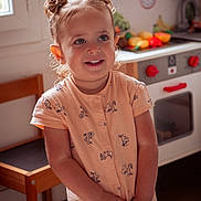 Léonore participe au concours pour gagner de l'argent avec cette photo : child, toddler, smiling, hair_buns, peach_dress, indoor, kitchen, toy_stove, play_food, wooden_chair, window_light, happy, cute, portrait, young_child, playtime, domestic, furniture, person, home