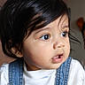 baby, child, face, portrait, close_up, curly_hair, denim_overalls, white_shirt, indoors, cute, expression, looking_away, young, skin, eyelashes, mouth_open, soft_light, infant, person, headshot