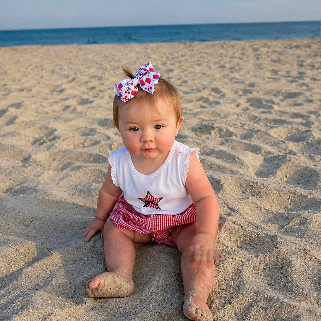 Kelly Kay joined the competition — help win amazing prizes! baby, barefoot, beach, bow, child, cute, footprints, happy, nature, ocean, outdoor, portrait, red_shorts, sand, sitting, sky, star, summer, sunlight, white_shirt