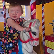 Kelly Kay joined the competition — help win amazing prizes! toddler, child, carousel, horse, ride, flowered_dress, indoor, playful, colorful, candy_striped_pole, yellow_wall, toy, amusement, fun, kid, portrait, cute, baby, face, hand