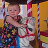 toddler, child, carousel, horse, ride, flowered_dress, indoor, playful, colorful, candy_striped_pole, yellow_wall, toy, amusement, fun, kid, portrait, cute, baby, face, hand
