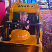 Kelly Kay is registered to the contest to win money with this photo: arcade, baby, carpet, child, colorful, cute, entertainment, fun, game_machine, happy, indoor, kid, person, playful, seat, steering_wheel, tonka, toy_truck, vehicle, yellow