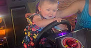 Kelly Kay is registered to the contest to win money with this photo: adult_arm, arcade, arcade_floor, car_seat, casual_clothing, child, colorful_lights, entertainment, family, fun, game_machine, gaming, indoor, joy, play, racing_game, smiling, steering_wheel, toddler, young_child