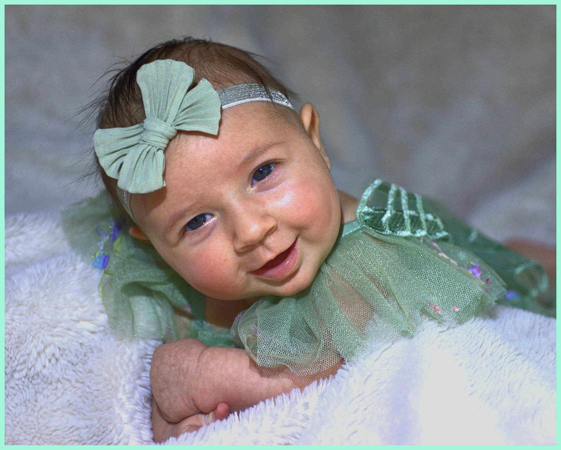 Harper joined the competition — help win amazing prizes! baby, infant, smile, bow_headband, green_dress, tulle, blanket, fluffy, cheeks, blue_eyes, portrait, closeup, adorable, happy, hand, skin, soft_texture, studio_style, cute, lying_down