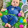 baby, child, easter_eggs, bunny_ears, blue_clothing, blanket, green_grass, tree_trunk, outdoor, grass, toy_carrot, colorful, infant, person, nature, spring, holiday, festive, cute, laying_down