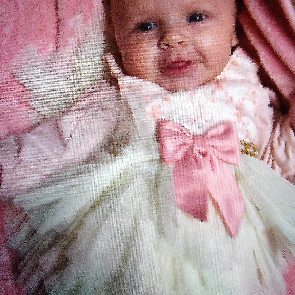 Jaelyn joined the competition — help win amazing prizes! baby, blanket, bonnet, clothing, costume, dress, face, fashion, formalwear, gown, happy, hat, head, laughing, newborn, person, photography, portrait, sitting, smile
