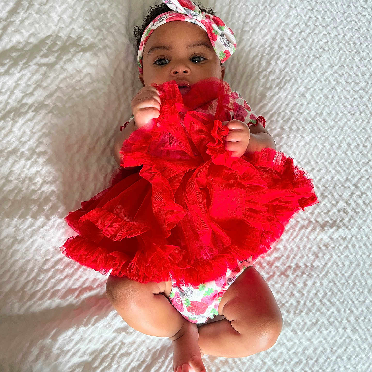 Kali joined the competition — help win amazing prizes! adorable, baby, barefoot, blanket, child, curly_hair, cute, fashion, headband, indoors, infant, lying_down, playful, portrait, red_dress, small_feet, small_hands, soft_lighting, toddler, white_bedspread