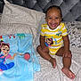Amarie joined the competition — help win amazing prizes! toddler, child, smiling, bed, blanket, pillow, jewelry, bracelet, earrings, yellow_clothing, striped_shirt, floral_bedding, tufted_headboard, indoors, happy, sitting, face, person, cute, playful