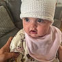 baby, infant, hat, knitted_hat, pink_bib, cute, wide_eyes, expression, indoor, living_room, sofa, person, child, hand, soft_lighting, face, clothing, cute_expression, holding, closeup
