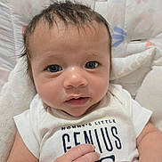 Dreux joined the competition — help win amazing prizes! baby, infant, face, eyes, hair, clothing, white_shirt, text_on_clothing, hands, skin, portrait, close_up, cute, child, sitting, soft_toys, fabric, patterned_background, indoor, young