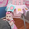 Scarlett joined the competition — help win amazing prizes! baby, girl, pink, headband, high_chair, banner, birthday, donut, floor, wooden_floor, furniture, curious, indoor, decor, celebration, child, clothing, person, standing, party