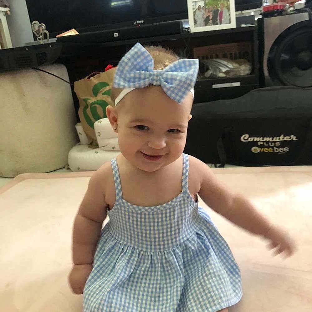 Acelyn joined the competition — help win amazing prizes! baby, blue_dress, bow_headband, carpet, child, cute, furniture, happy, headwear, home, indoor, infant, living_room, person, playful, portrait, sitting, smile, speaker, television