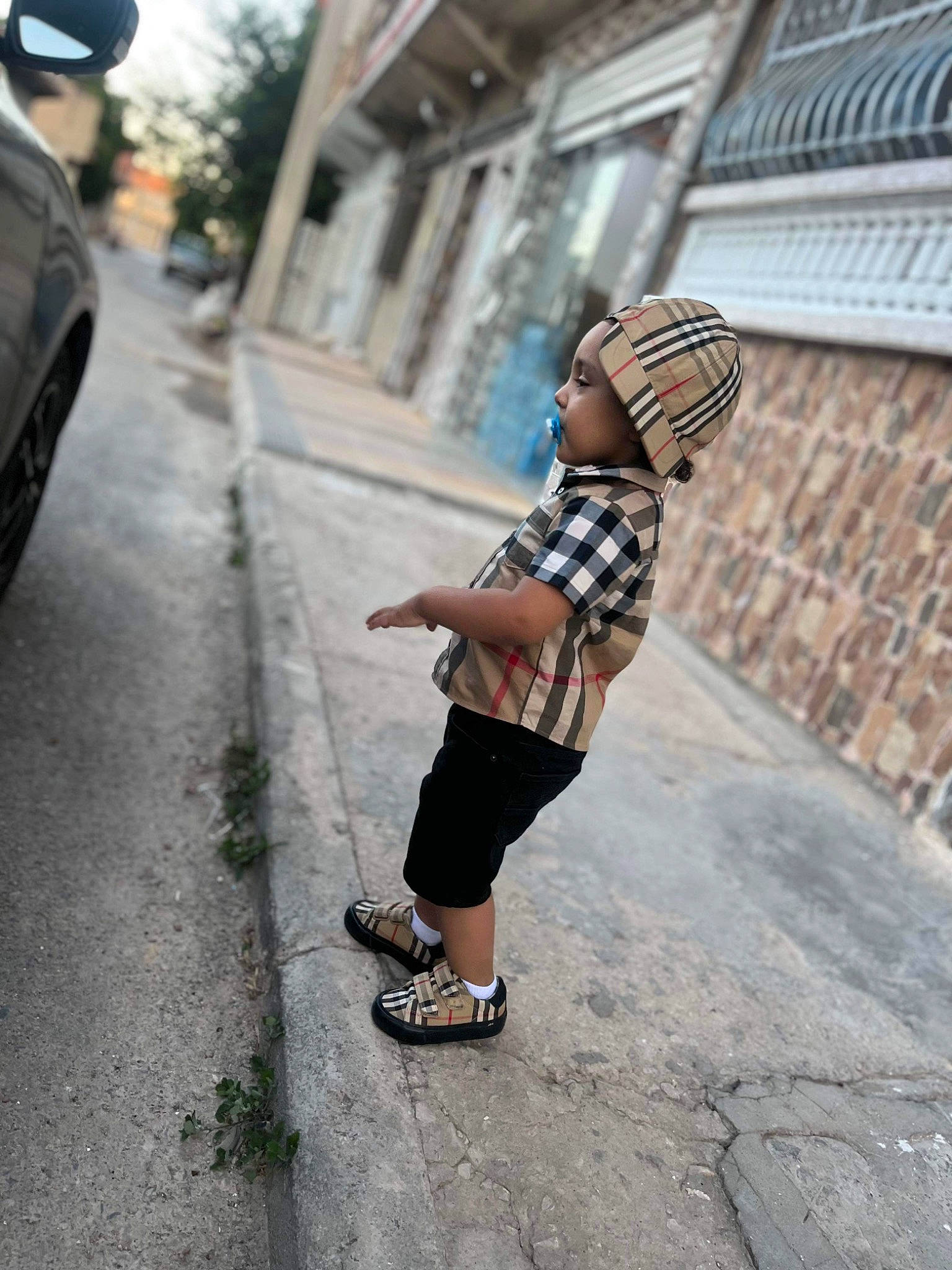 Imrân participe au concours pour gagner de l'argent avec cette photo : alley, asphalt, city, fashion_accessory, hat, headwear, human_leg, pattern, pedestrian, person, plaid, public_space, road, road_surface, shorts, sidewalk, sleeve, street, tartan, toddler