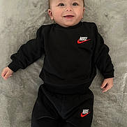 Ilan a rejoint le concours — aidez-le/la à gagner de superbes lots ! baby, smiling, black_clothing, nike_logo, infant, lying_down, blanket, cute, happy, child, face, sleeves, pants, soft_texture, portrait, young_child, indoor, casual_wear, person, comfortable