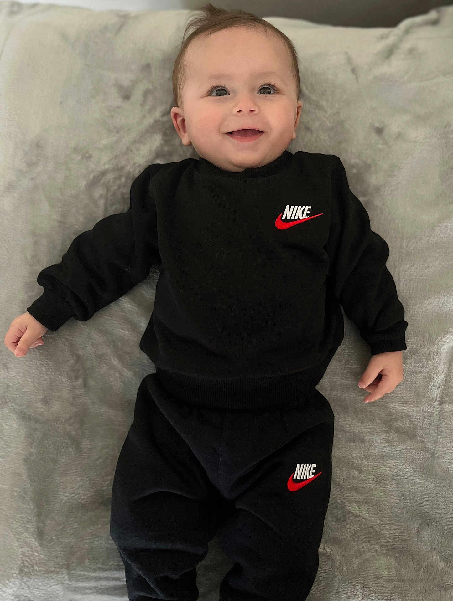 Ilan a rejoint le concours — aidez-le/la à gagner de superbes lots ! baby, smiling, black_clothing, nike_logo, infant, lying_down, blanket, cute, happy, child, face, sleeves, pants, soft_texture, portrait, young_child, indoor, casual_wear, person, comfortable