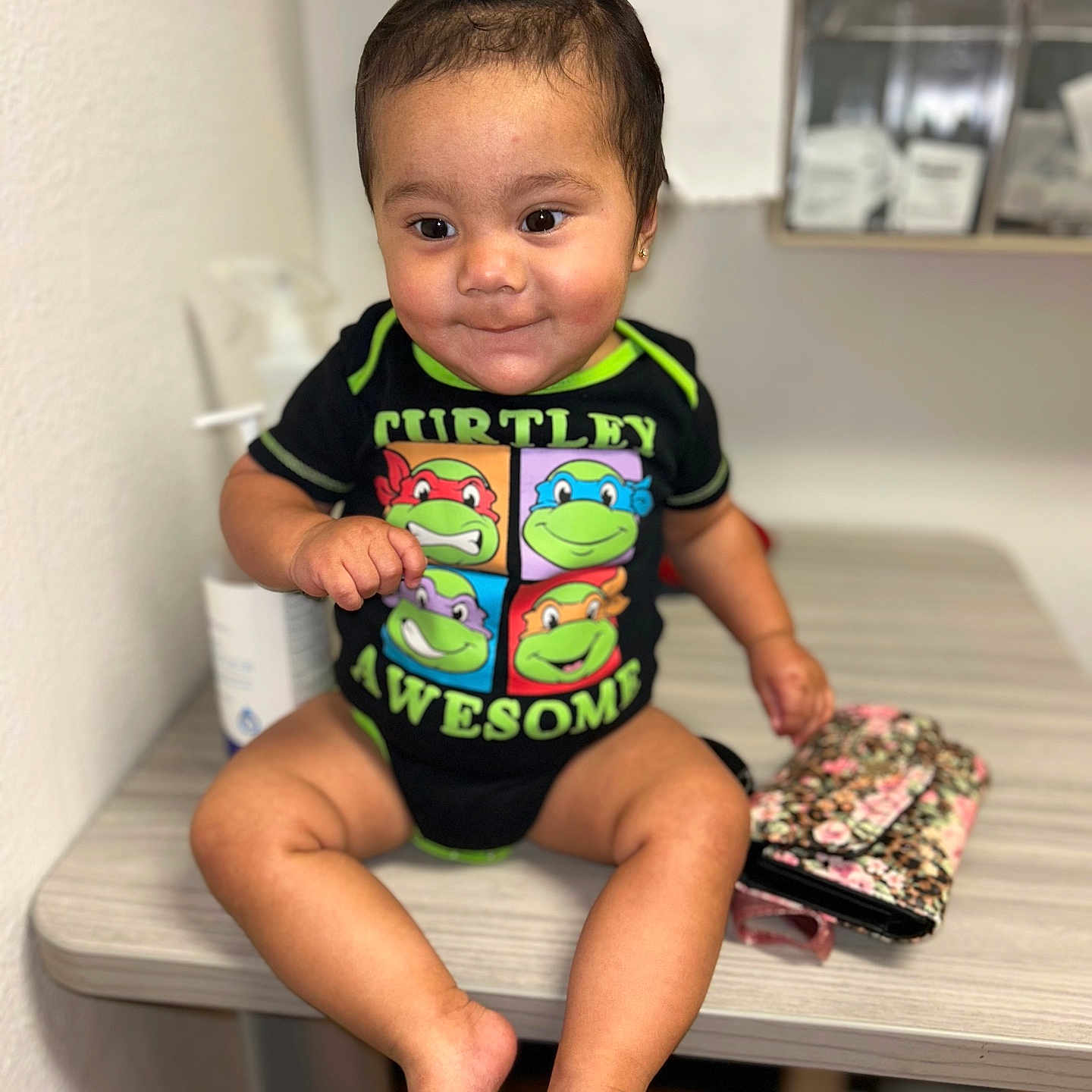 Jenicka joined the competition — help win amazing prizes! baby, child, colorful_clothing, cute, expression, face, footwearless, furniture, hand, happy, indoor, onesie, person, ponytail, sitting, skin, smiling, table, wallet, young_child