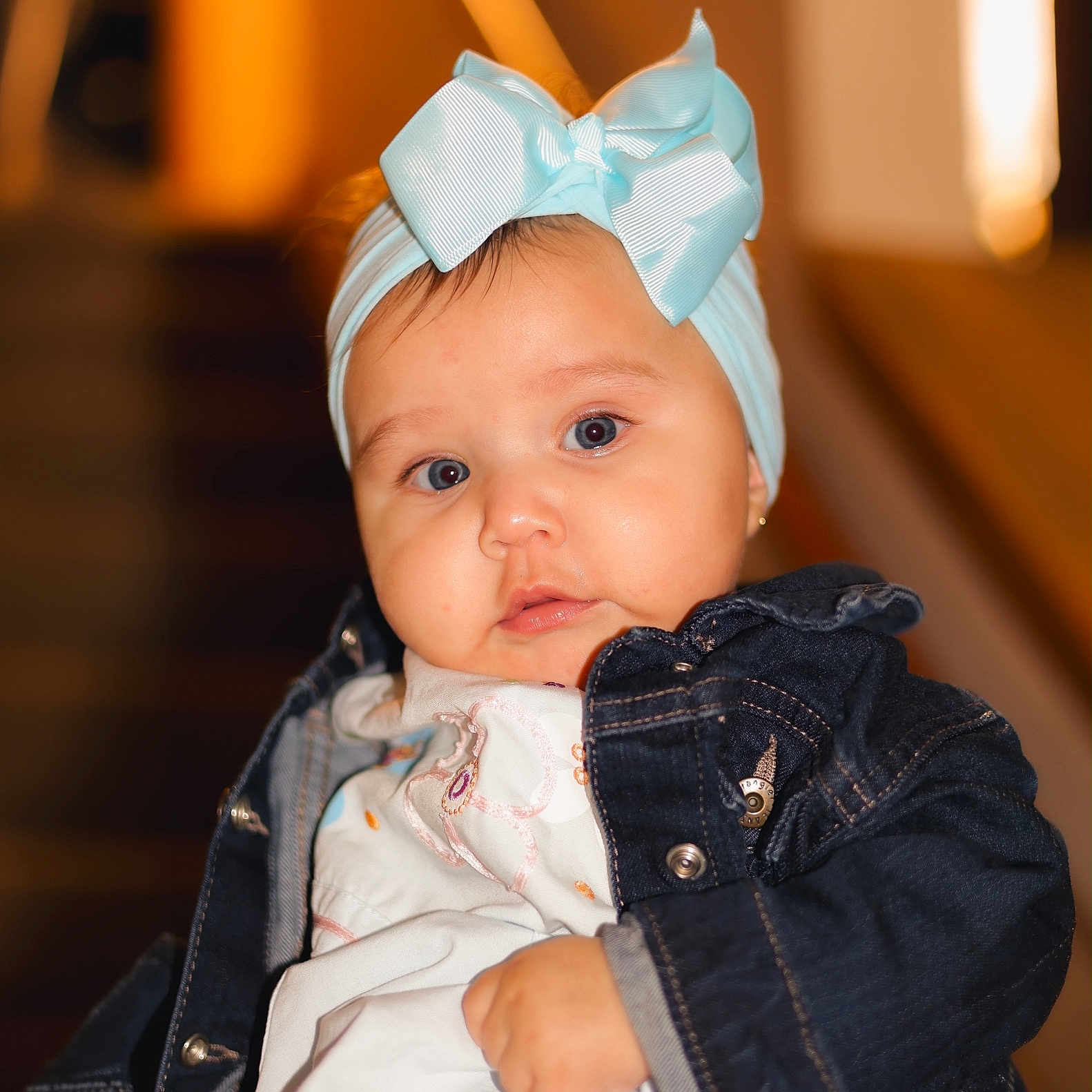 Nelsy joined the competition — help win amazing prizes! baby, child, infant, portrait, face, wide_eyed, blue_eyes, headband, bow, denim_jacket, clothing, sitting, indoor, warm_lighting, close_up, photography, blurred_background, cute, fashion, person