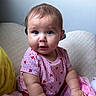 baby, child, infant, portrait, sitting, indoors, smiling, curious, serious_expression, face, eyes, pink_clothing, strawberry_pattern, plush_toy, stuffed_animal, blanket, cushion, cozy, home, photography