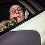 person, dog, car, glasses, window, night, surprised, peeking, fur, pet, animal, vehicle, face, ears, nose_ring, dark_background, closeup, expression, two_subjects, indoor