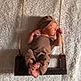 newborn, baby, sleeping, swing, rope, wood, brown_clothing, hat, blanket, cozy, infant, peaceful, portrait, soft_texture, indoor, cute, resting, small_feet, child, warm_lighting