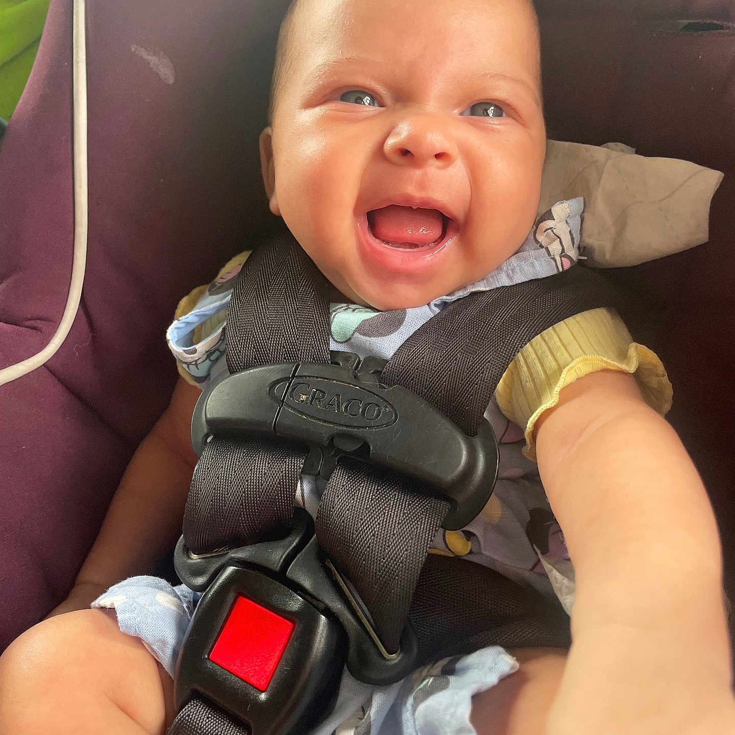 Aniyah is registered to the contest to win money with this photo: baby, infant, child, smiling, happy, laughing, face, portrait, car_seat, safety_harness, seatbelt, vehicle, indoor, close_up, sitting, blue_clothing, yellow_sleeve, brown_eyes, infant_carrier, joy
